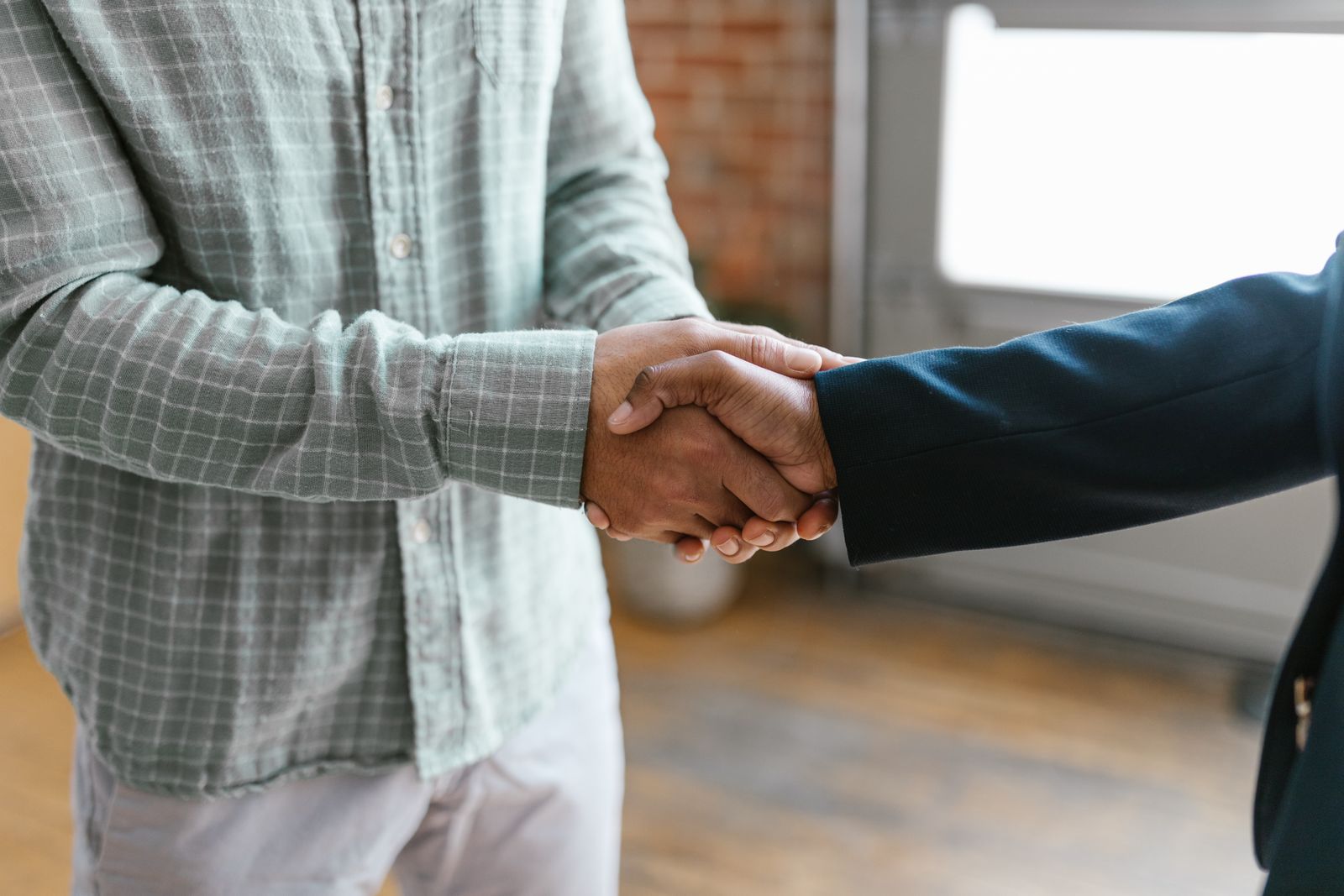 Two people shaking hands, a plaid sleeve and a dark blazer sleeve