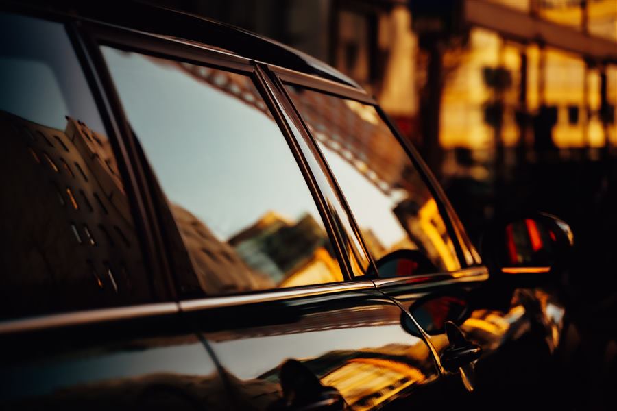 Warm evening light reflected in the tinted windows of a black car