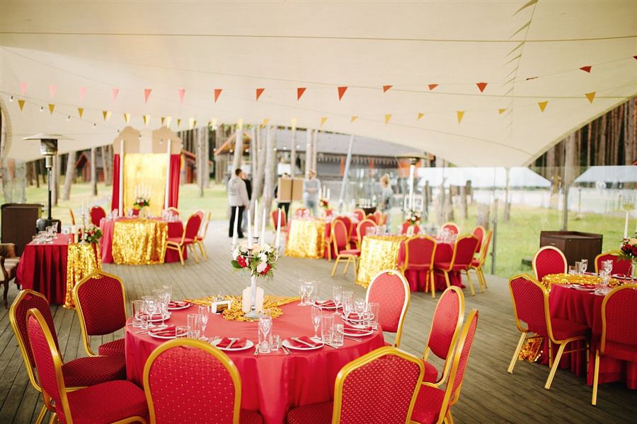 An outdoor reception under a tent with red and gold decor